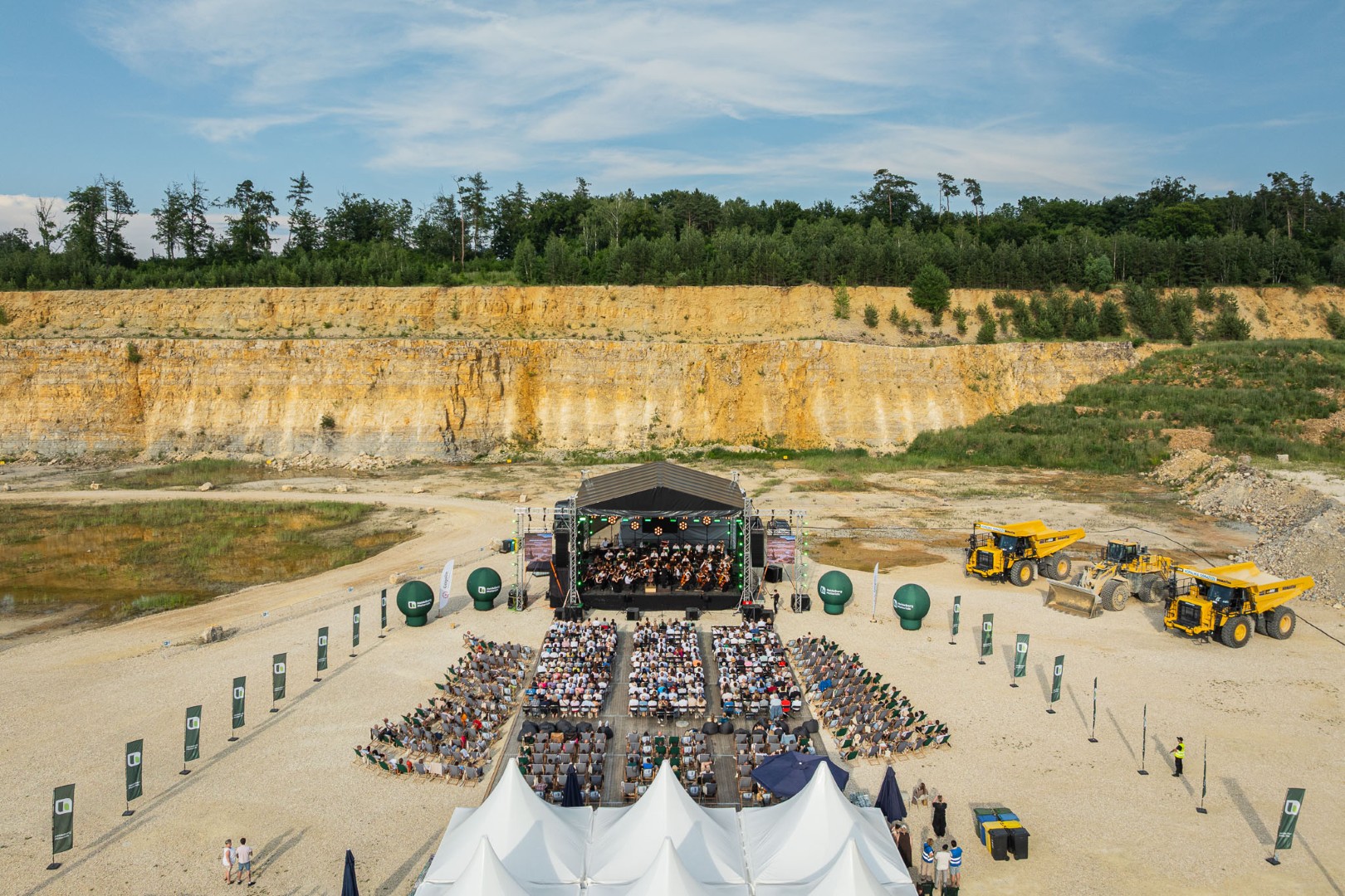 Widok na koncert plenerowy w kamieniołomie, z dużą sceną, publicznością i sprzętem przemysłowym w tle.
